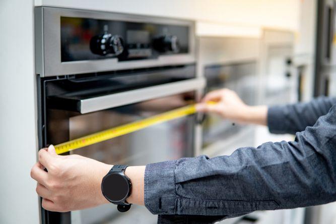 man measuring the oven with a yellow measuring tape