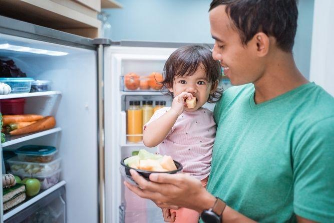 father holding daughter near the open fridge