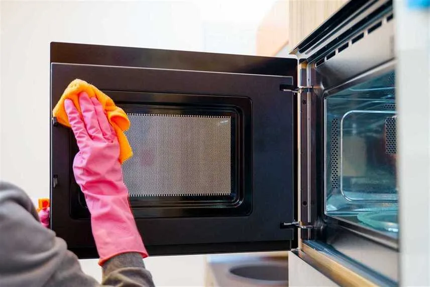 Image of woman hands in rubber gloves washing microwave in kitchen