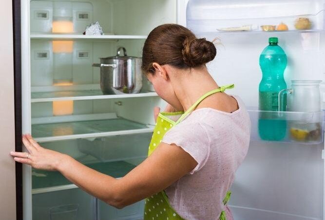 woman looks inside the fridge in green apron