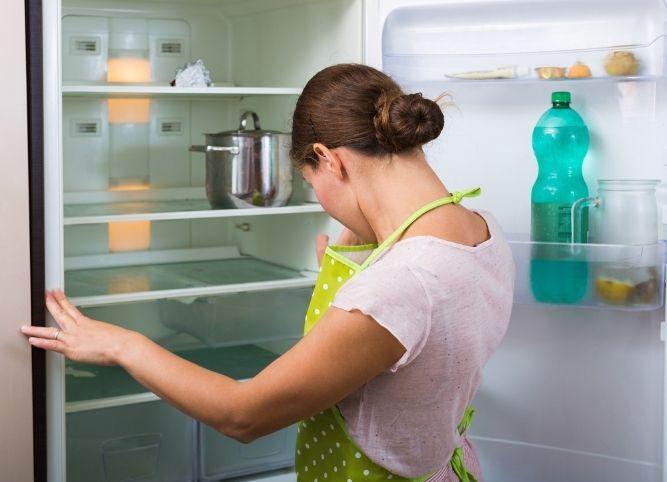 woman looks inside the fridge in green apron