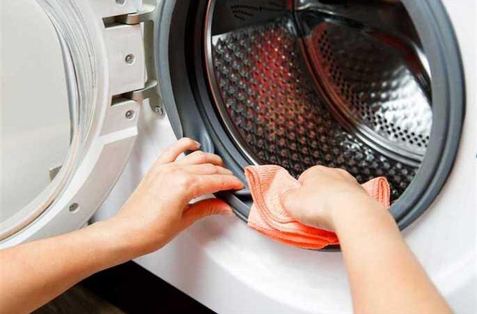 person cleaning a washing machine with orange cloth