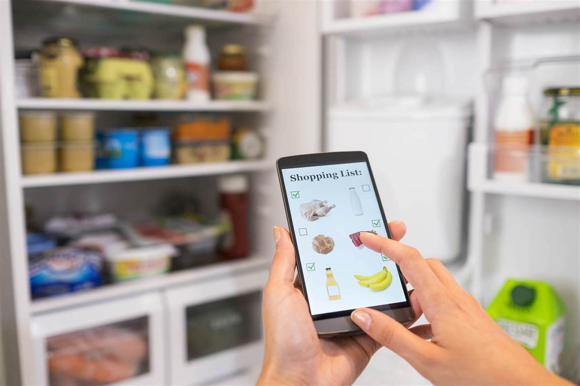 a person checking shopping list on a smartphone in front of the open fridge